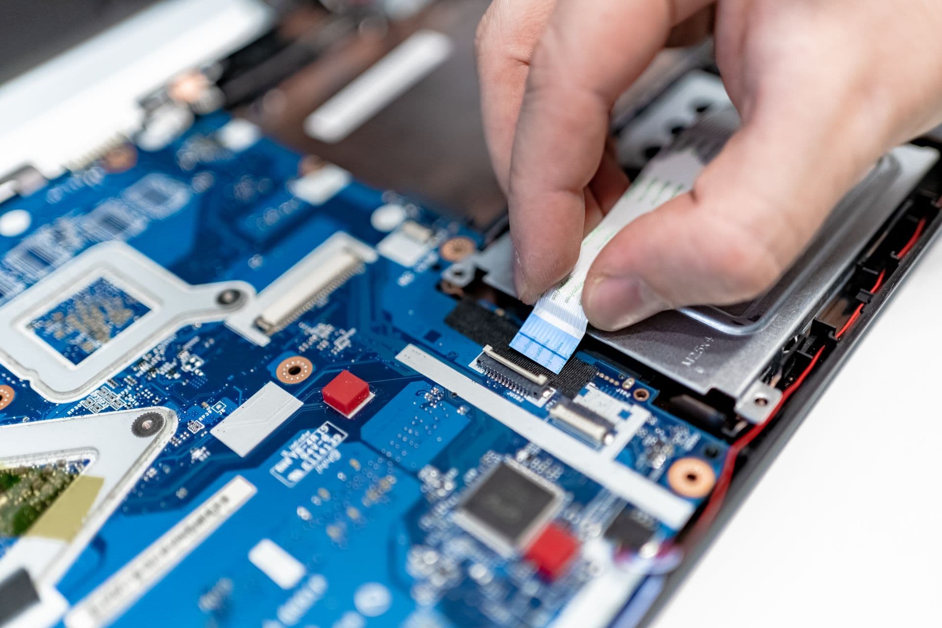 Technician connecting a ribbon cable inside an open laptop during a repair